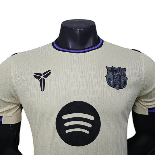 GOATkitz Barcelona 2025-26 away jersey in cream with black and purple accents. Features Kobe logo, FCB crest, and Spotify logo.