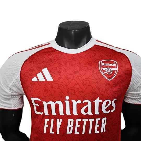 GOATkitz Arsenal 2025-26 player version home jersey in red with white sleeves and subtle repeating Arsenal crest pattern.
