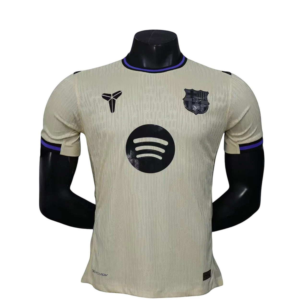 GOATkitz Barcelona 2025-26 away jersey in cream with black Spotify logo and Kobe Bryant logo. Features purple trim on collar and sleeves.
