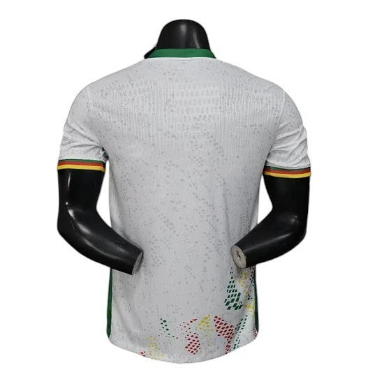 GOATkitz Cameroon 2026 player version away jersey, white with green collar and armbands in yellow, red, and green. Features subtle textured pattern.