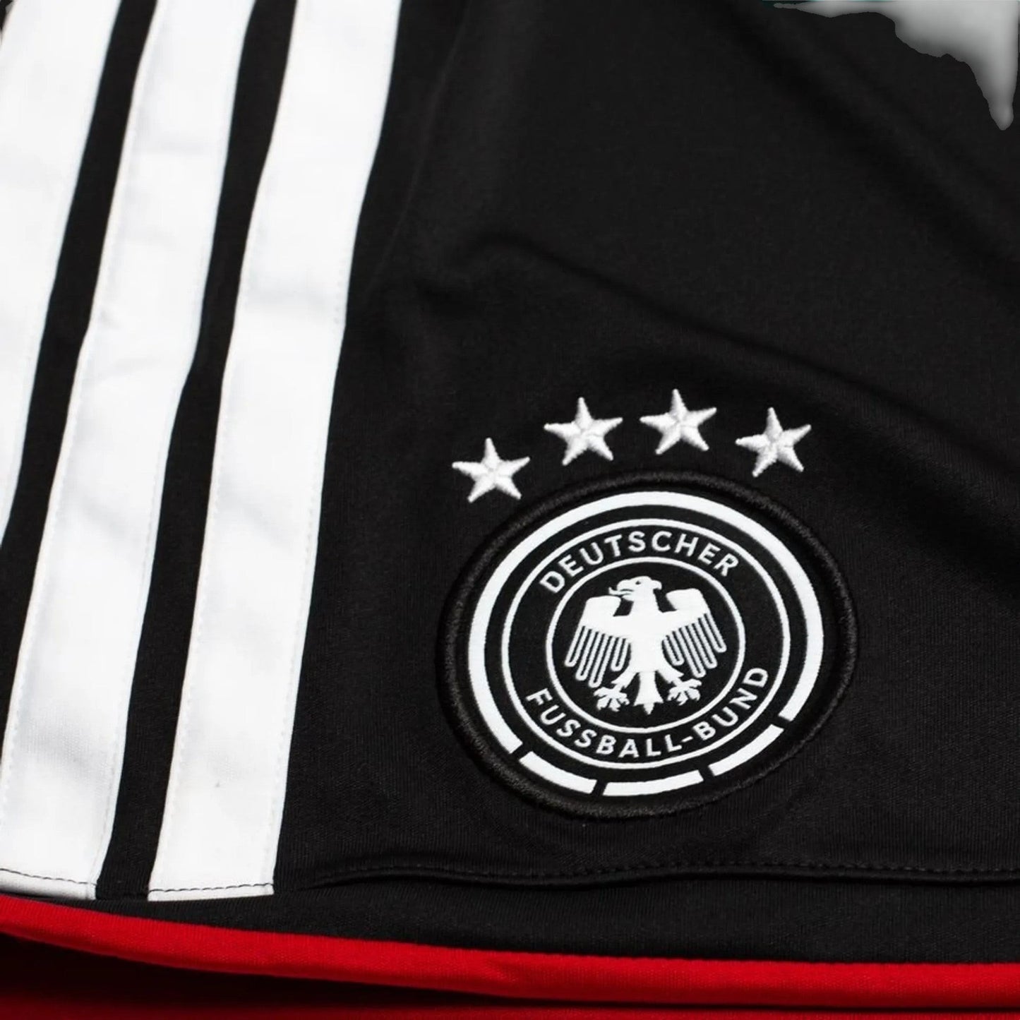GOATkitz Germany 2026 kids home jersey detail with black fabric, white stripes, embroidered crest, and four stars.