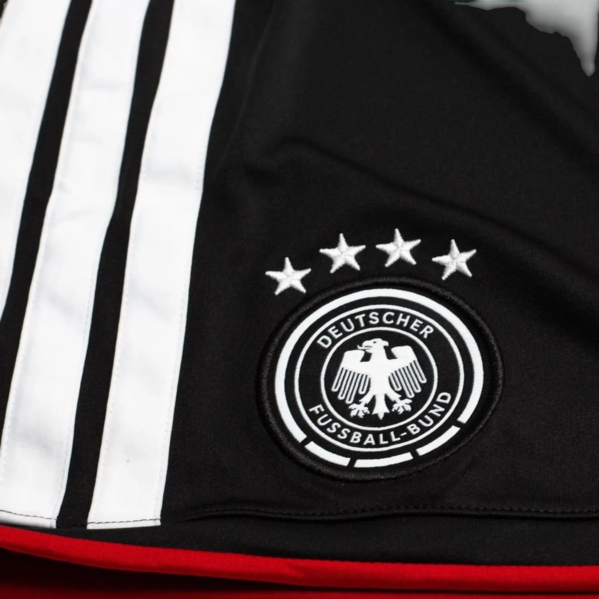 GOATkitz Germany 2026 kids home jersey detail with black fabric, white stripes, embroidered crest, and four stars.