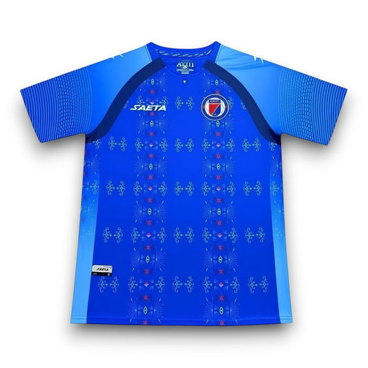 GOATkitz Haiti 2026 adult home jersey in blue with a repeating geometric pattern and Haiti crest. Short sleeves with striped detail.