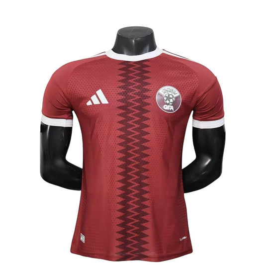 GOATkitz Qatar 2026 player version home jersey in maroon with white trim and zigzag pattern. Features QFA crest and Adidas logo.