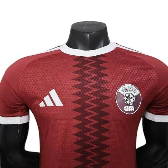 GOATkitz maroon Qatar 2026 player version soccer jersey with white Adidas stripes and QFA crest. Features a zigzag pattern.